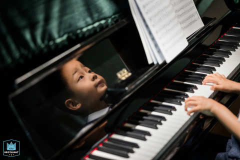 Taken in Hangzhou City, Zhejiang, this candid family photo captures a young boy playing the piano with his hands on the keys, as his face is reflected in the mirror finish of the black instrument.